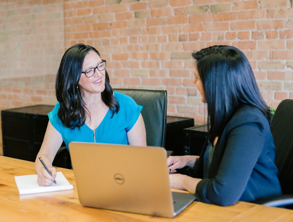 woman in teal t-shirt sitting beside woman in suit jacket